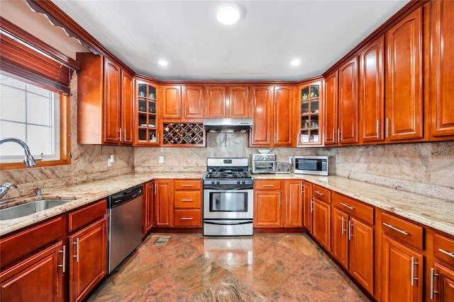 kitchen featuring light stone counters, a sink, appliances with stainless steel finishes, backsplash, and under cabinet range hood