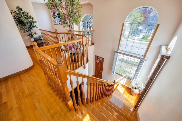 stairs with baseboards, wood finished floors, and a high ceiling