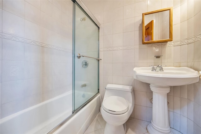 bathroom featuring enclosed tub / shower combo, toilet, tile patterned flooring, and tile walls