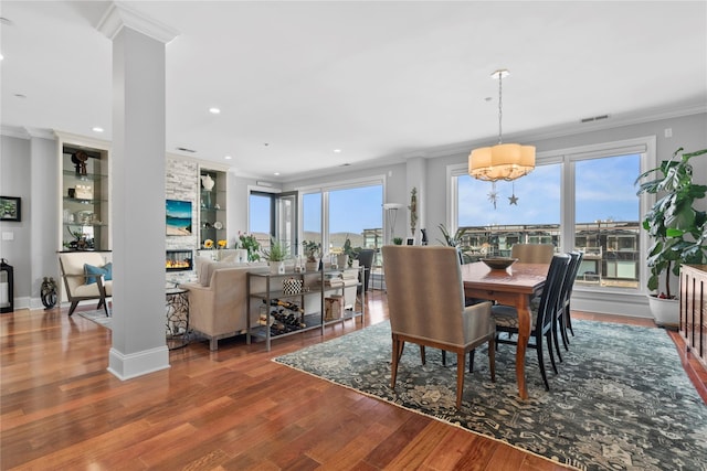 dining area with crown molding, an inviting chandelier, wood finished floors, recessed lighting, and a large fireplace