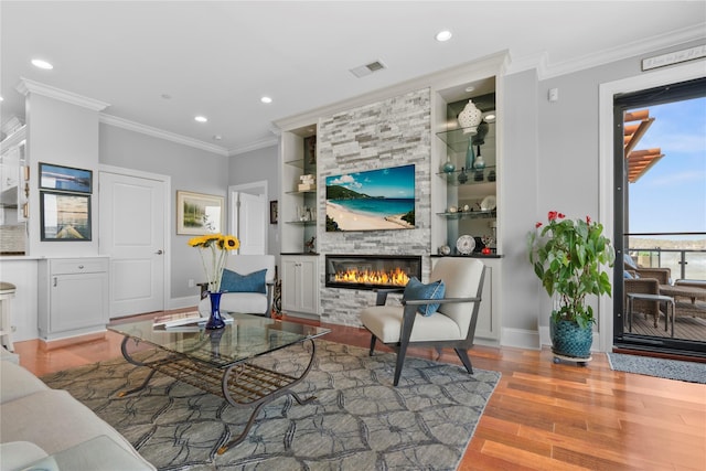 living area with visible vents, built in features, wood finished floors, baseboards, and a large fireplace