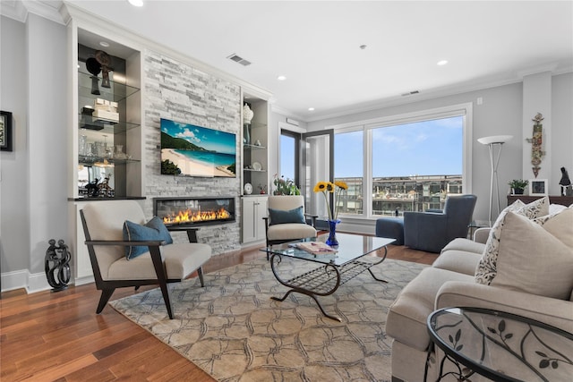 living room with a stone fireplace, ornamental molding, built in features, and wood finished floors