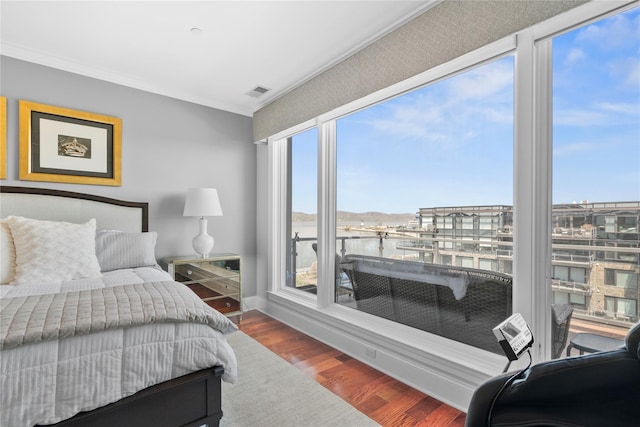 bedroom with visible vents, crown molding, wood finished floors, baseboards, and a water view