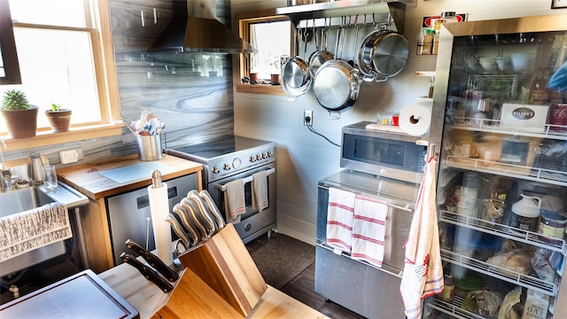 kitchen featuring a wealth of natural light, wall chimney exhaust hood, appliances with stainless steel finishes, and butcher block counters