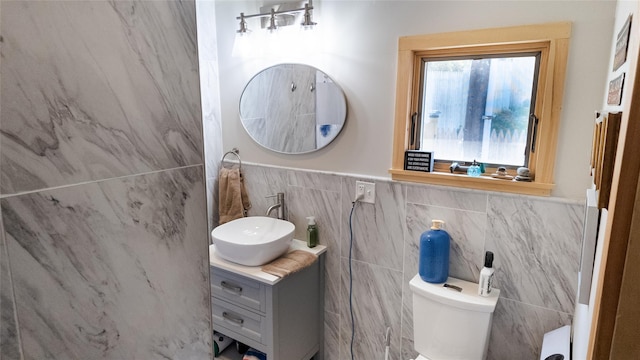 bathroom with toilet, tile walls, wainscoting, and vanity
