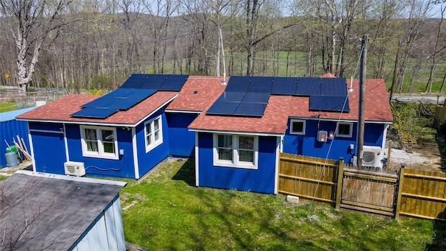 view of front of property with a front yard, a shingled roof, a view of trees, solar panels, and fence