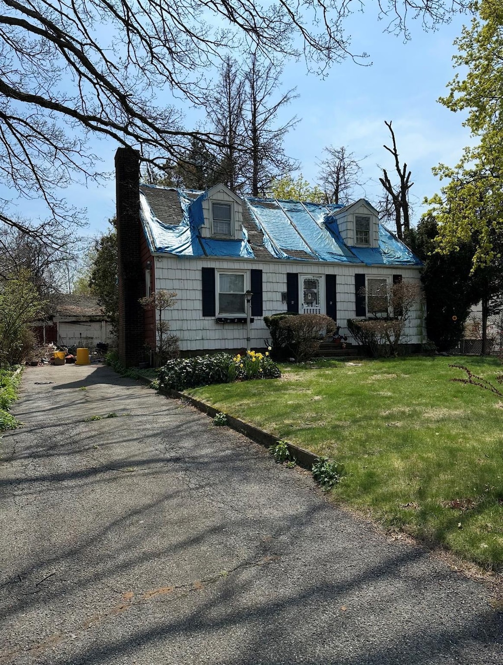cape cod house with a chimney, driveway, and a front lawn