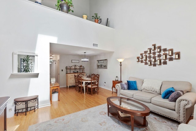 living room featuring baseboards, light wood-style flooring, a high ceiling, and visible vents
