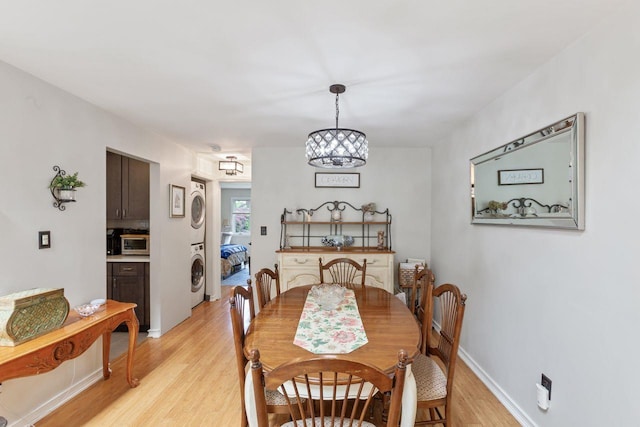 dining space with baseboards, stacked washer and dryer, light wood-style flooring, and a notable chandelier