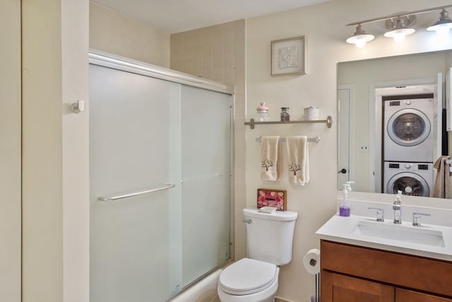 bathroom featuring vanity, stacked washer and clothes dryer, a shower with shower door, and toilet