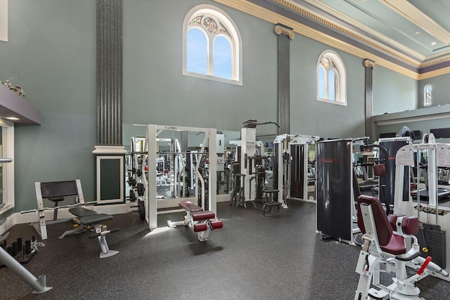 gym with a healthy amount of sunlight, crown molding, and a towering ceiling