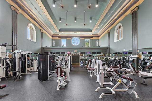 exercise room featuring crown molding, plenty of natural light, a raised ceiling, and a towering ceiling