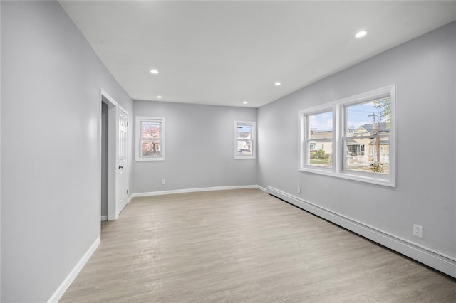 empty room with light wood-style floors, baseboard heating, a wealth of natural light, and baseboards