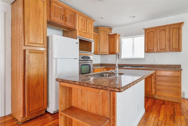 kitchen featuring a kitchen island with sink, dark stone counters, a sink, light wood finished floors, and appliances with stainless steel finishes