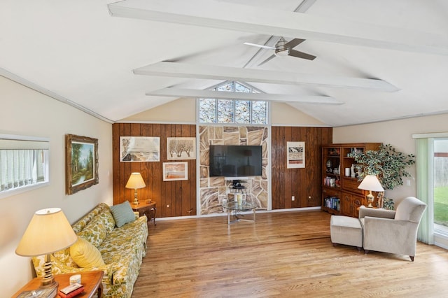 living area with ceiling fan, vaulted ceiling with beams, wood walls, and wood finished floors