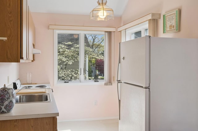 kitchen with freestanding refrigerator, a sink, brown cabinets, and light countertops