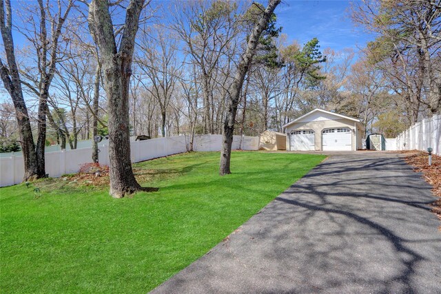 view of yard featuring driveway, fence private yard, an outdoor structure, and a detached garage