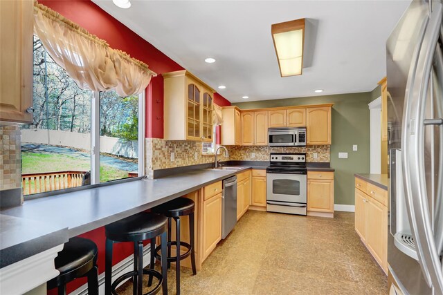 kitchen featuring light brown cabinets, a sink, decorative backsplash, light floors, and stainless steel appliances