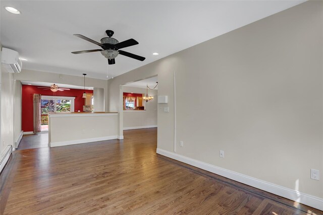 unfurnished living room with a wall unit AC, baseboards, ceiling fan with notable chandelier, baseboard heating, and wood finished floors