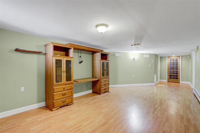 unfurnished living room with light wood-type flooring, baseboards, built in desk, and visible vents