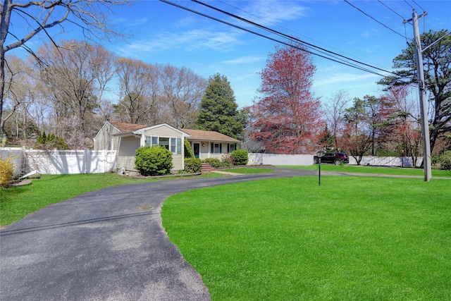 ranch-style home featuring a front lawn, fence, and aphalt driveway