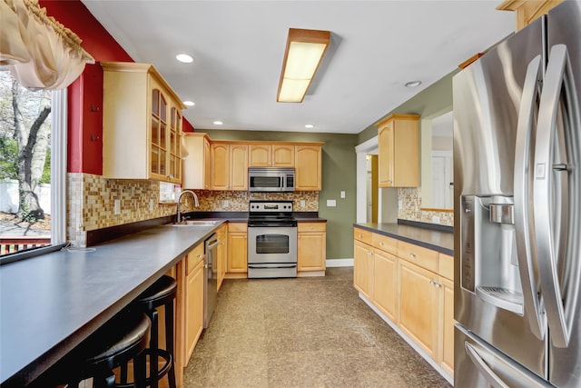 kitchen with dark countertops, light brown cabinetry, stainless steel appliances, and a sink
