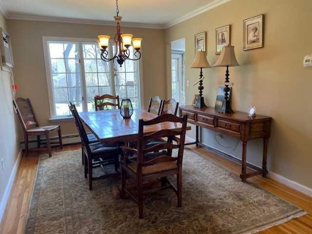 dining area featuring a chandelier, ornamental molding, baseboard heating, and wood finished floors