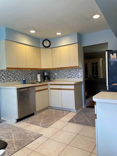 kitchen with backsplash, dishwasher, light countertops, freestanding refrigerator, and cream cabinetry