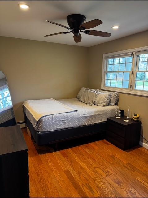bedroom with wood finished floors, baseboards, a baseboard radiator, recessed lighting, and a ceiling fan