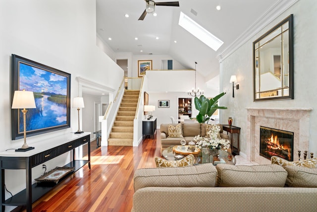 living room with a high end fireplace, ceiling fan with notable chandelier, wood finished floors, high vaulted ceiling, and stairs