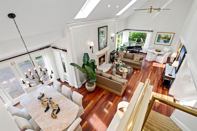 living area with wood finished floors, a skylight, ceiling fan with notable chandelier, a fireplace, and high vaulted ceiling