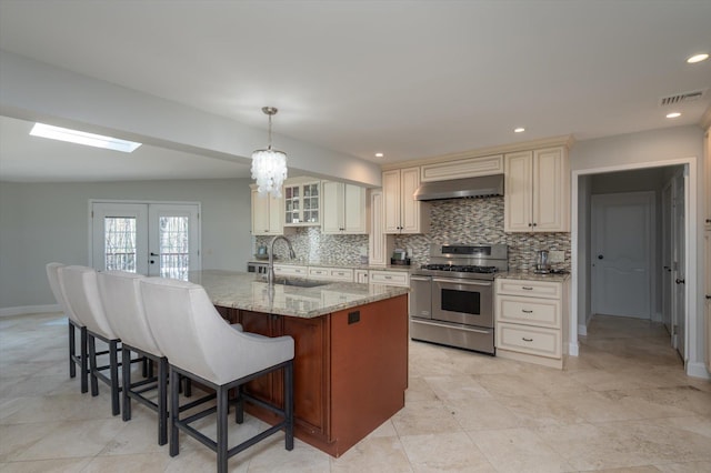 kitchen featuring ventilation hood, visible vents, a sink, double oven range, and cream cabinets