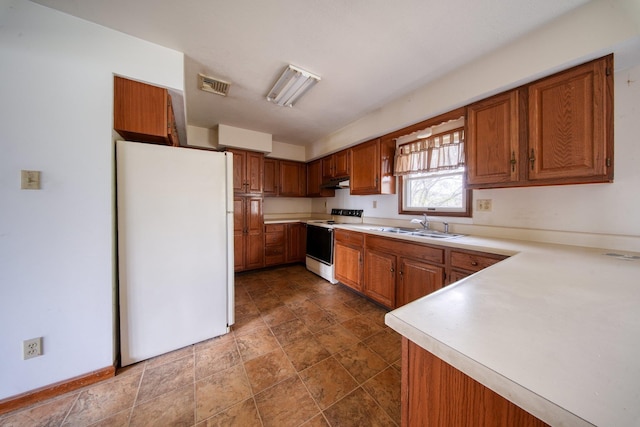 kitchen with white appliances, brown cabinets, visible vents, and a sink