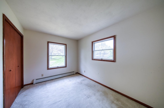unfurnished bedroom featuring light colored carpet, baseboards, a baseboard heating unit, and a closet