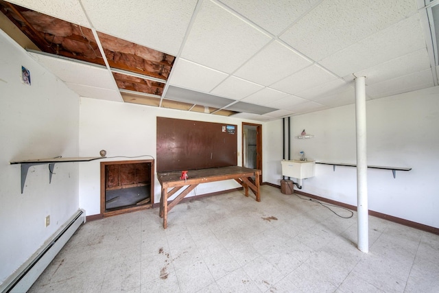 basement featuring light floors, baseboards, baseboard heating, and a drop ceiling