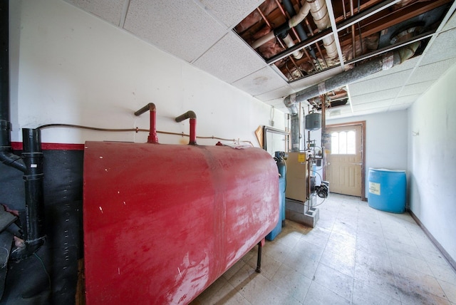 basement with baseboards, tile patterned floors, heating fuel, and a paneled ceiling