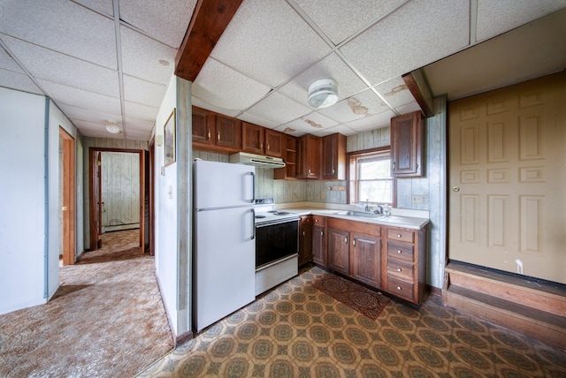 kitchen featuring light countertops, under cabinet range hood, a drop ceiling, white appliances, and dark carpet