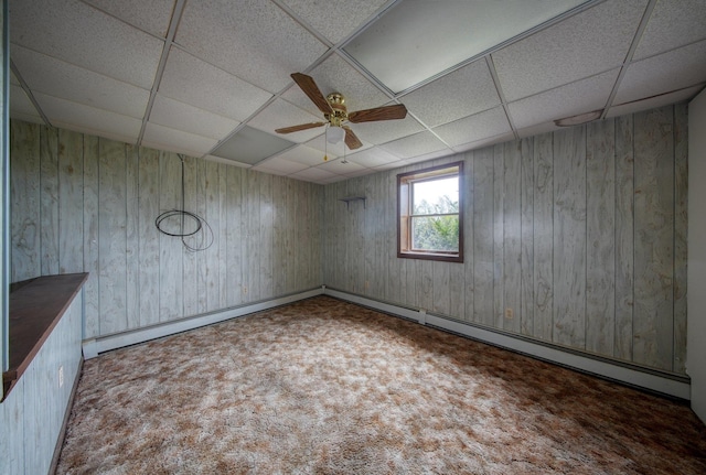 spare room featuring carpet floors, a ceiling fan, a paneled ceiling, and wood walls