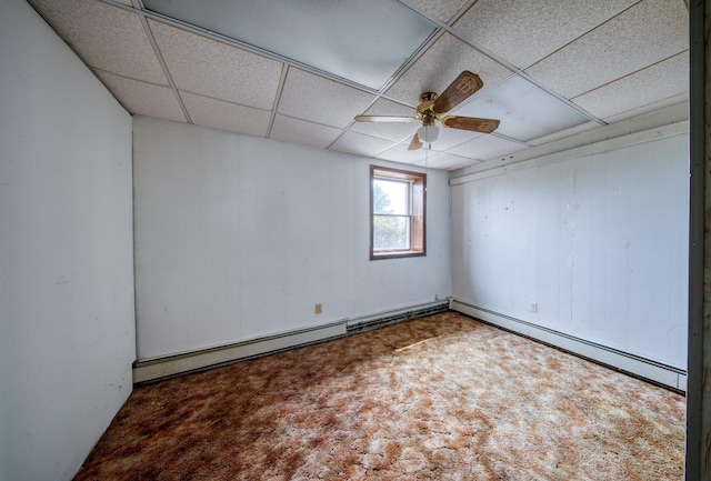 unfurnished room featuring carpet floors, ceiling fan, a drop ceiling, wooden walls, and baseboard heating