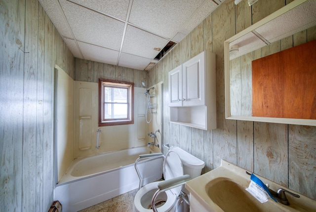 bathroom featuring wood walls, a paneled ceiling, shower / bathtub combination, and toilet