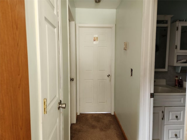 corridor featuring dark carpet and baseboards