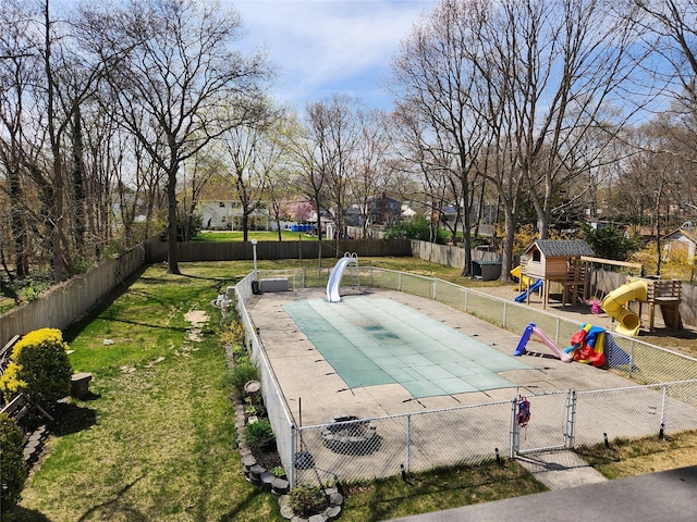 view of swimming pool with a water slide, a gate, playground community, fence private yard, and a lawn