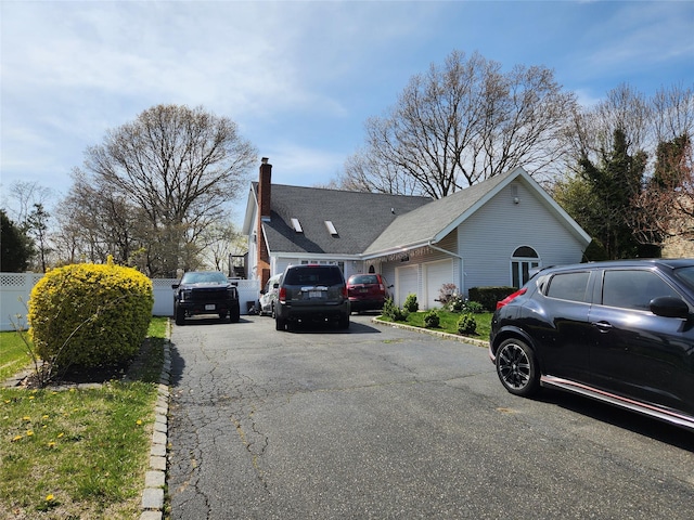 view of side of home featuring a chimney, fence, aphalt driveway, and a garage