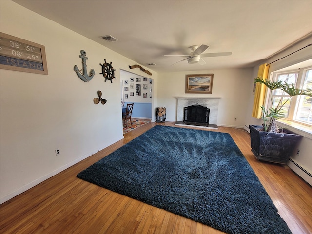 living room with baseboards, visible vents, wood finished floors, a brick fireplace, and ceiling fan