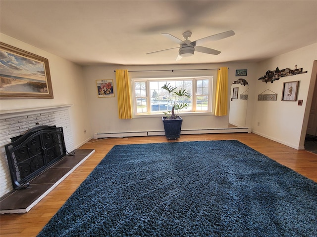 unfurnished living room featuring a baseboard radiator, wood finished floors, ceiling fan, and a fireplace