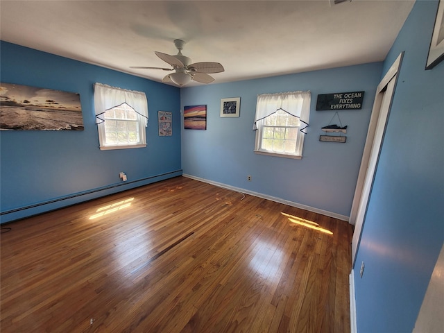 unfurnished room featuring a baseboard radiator, wood finished floors, a wealth of natural light, and a ceiling fan