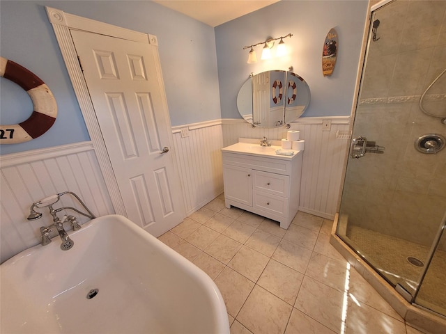 bathroom with a wainscoted wall, a stall shower, a freestanding tub, tile patterned flooring, and vanity