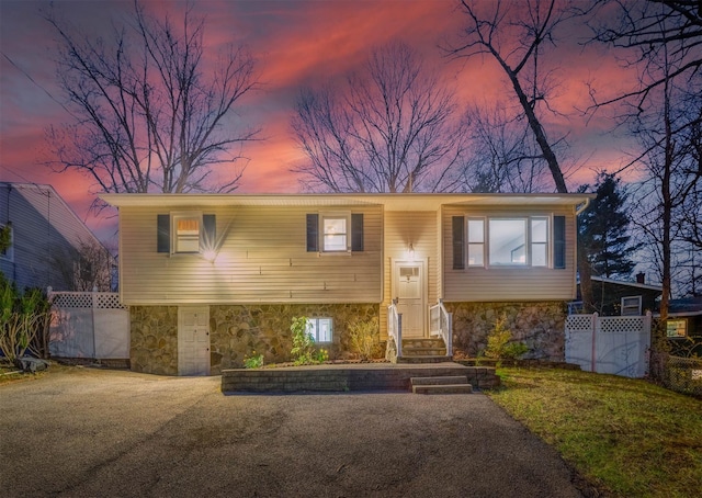 bi-level home with stone siding, entry steps, and fence