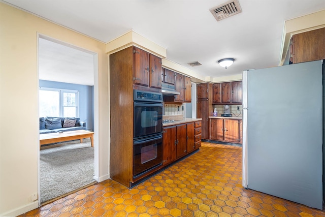 kitchen with black appliances, visible vents, under cabinet range hood, and light countertops