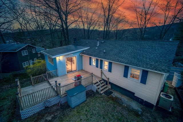 view of front facade with a wooden deck, cooling unit, and roof with shingles